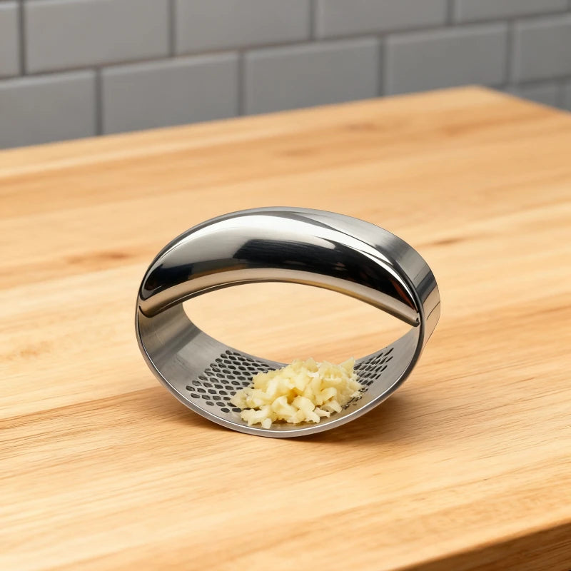 Stainless steel manual garlic press held over a cutting board with minced garlic.