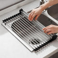 Black roll-up dish drying rack draped over a kitchen sink with dishes drying above it.