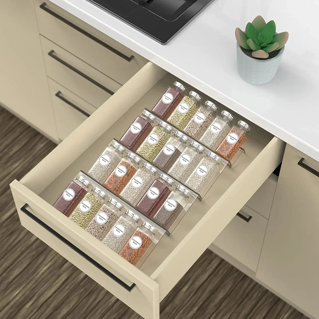 Adjustable acrylic spice organizer tray inside an open kitchen drawer holding spice jars at an angle.