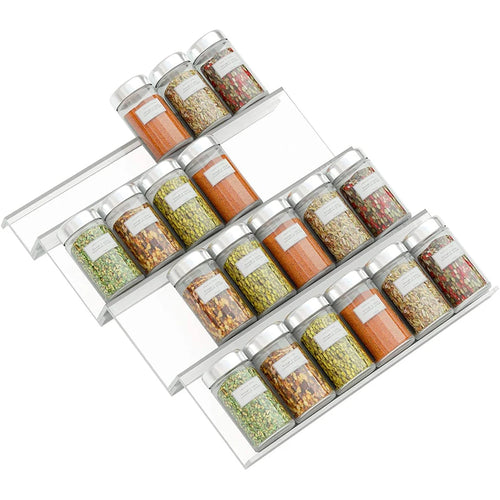 Adjustable acrylic spice organizer tray inside an open kitchen drawer holding spice jars at an angle.