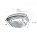 Stainless steel manual garlic press held over a cutting board with minced garlic.