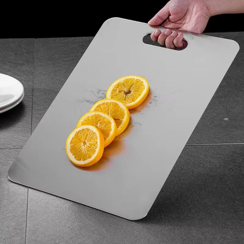 Stainless steel antibacterial cutting board on a kitchen counter with sliced vegetables.